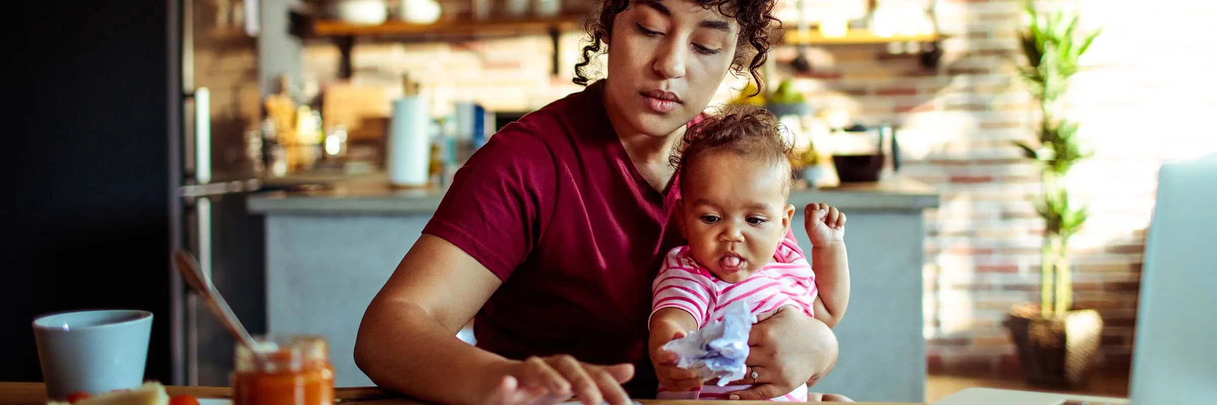 woman and a baby sitting at the kitchen table with a calculator and laptop