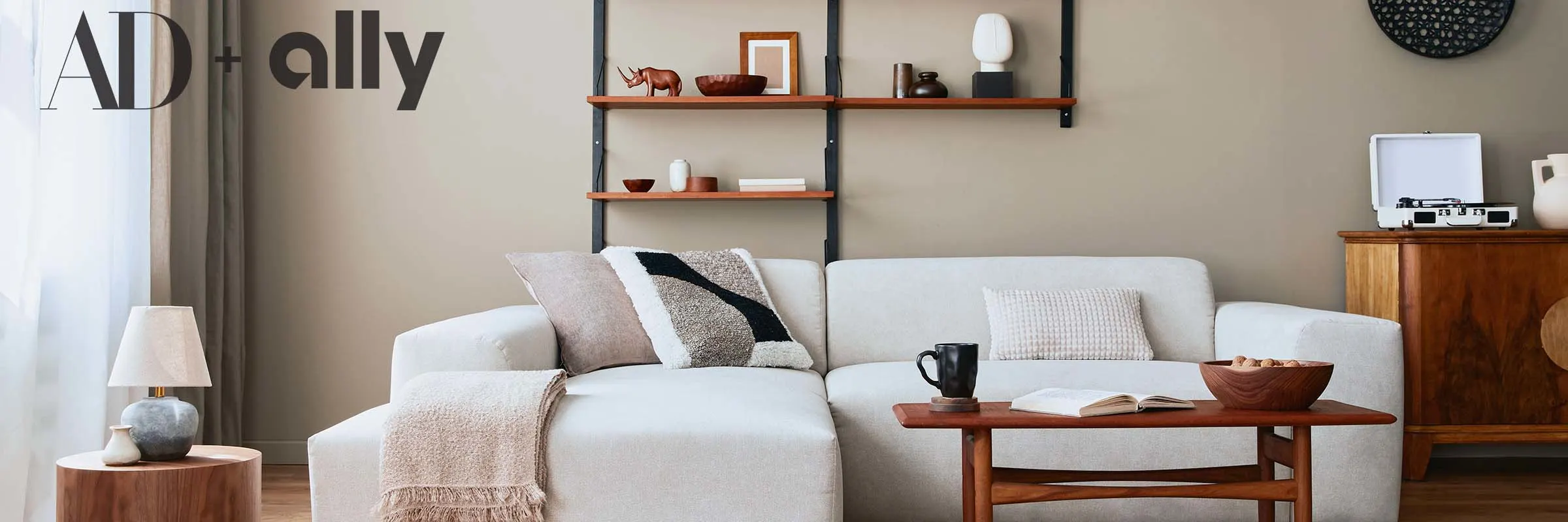 Modern living rom with a beige sofa, coffee table, shelf with d&eacute;cor, pendant lamp and small decorations.