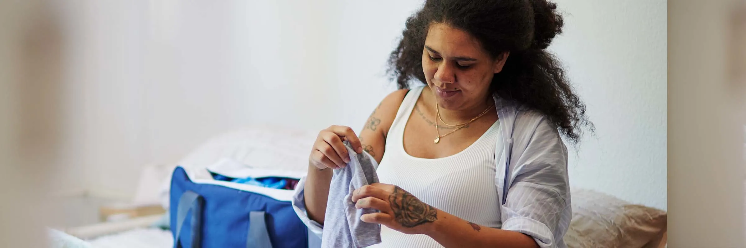 A pregnant woman is sitting on a bed and sorting baby clothes.