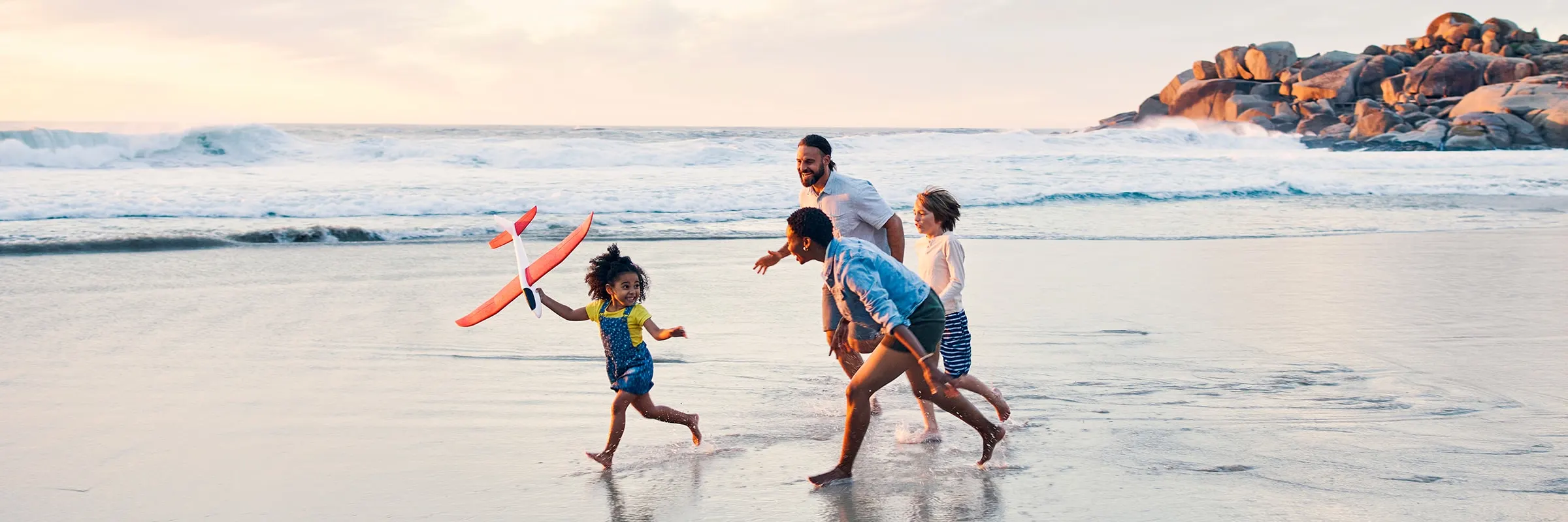  Family of four runs on the beach, playing with a toy airplane