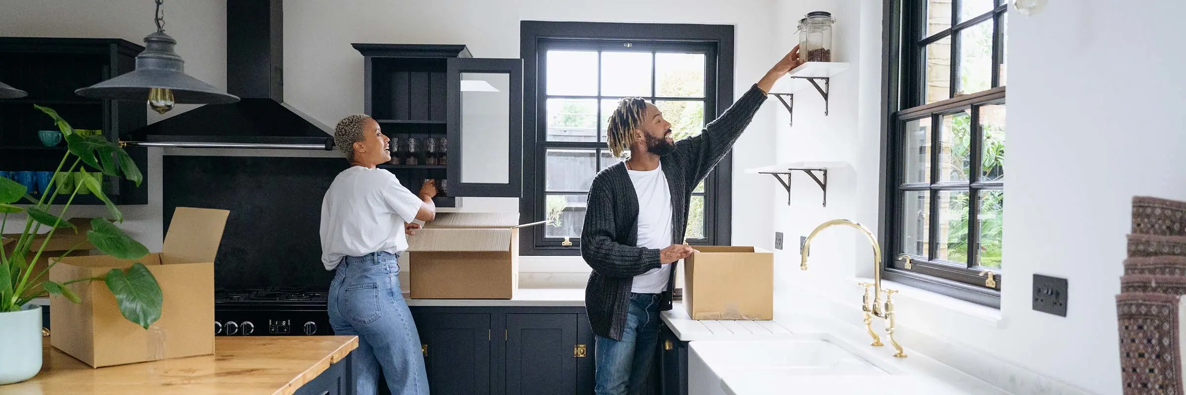 A man and woman are unpacking boxes and placing items in their new kitchen.