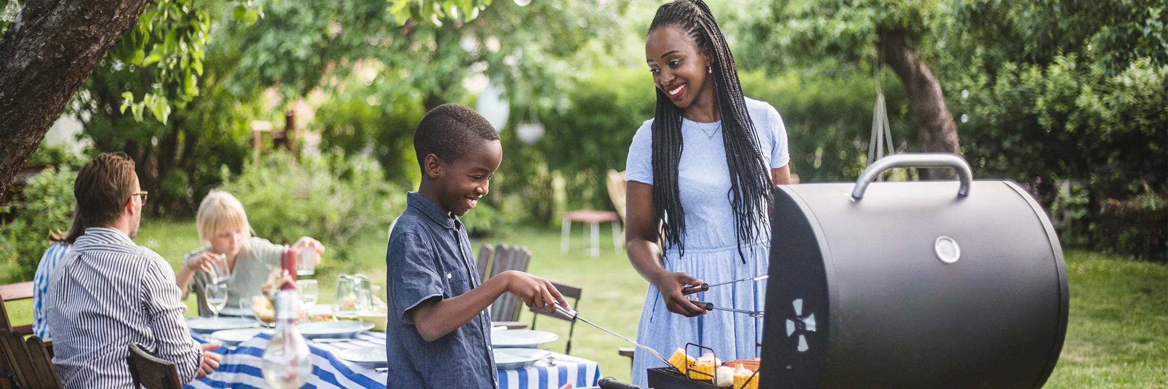 Mother and child happily cooking on a grill together outside.
