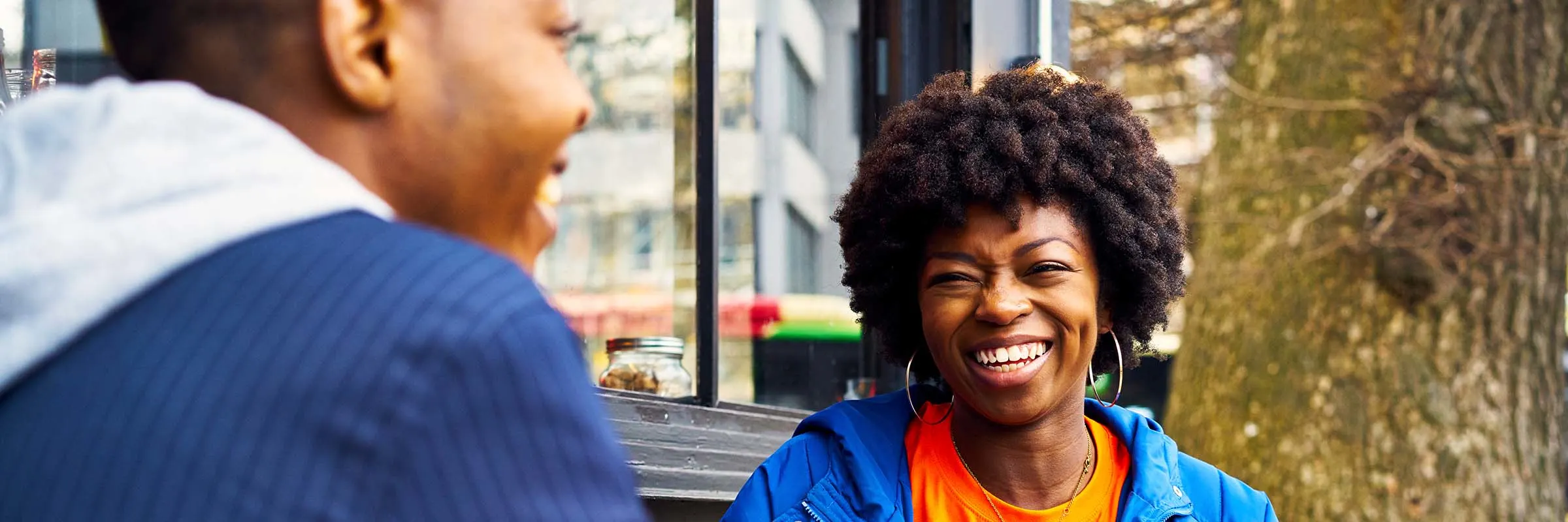 Young woman is smiling while having coffee with a man at an outdoor table.