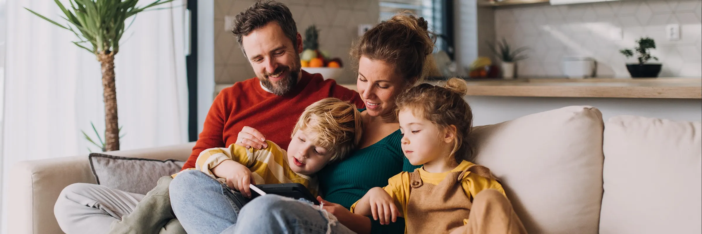 A  happy mother and father sit on a couch in a living room with their two young children.