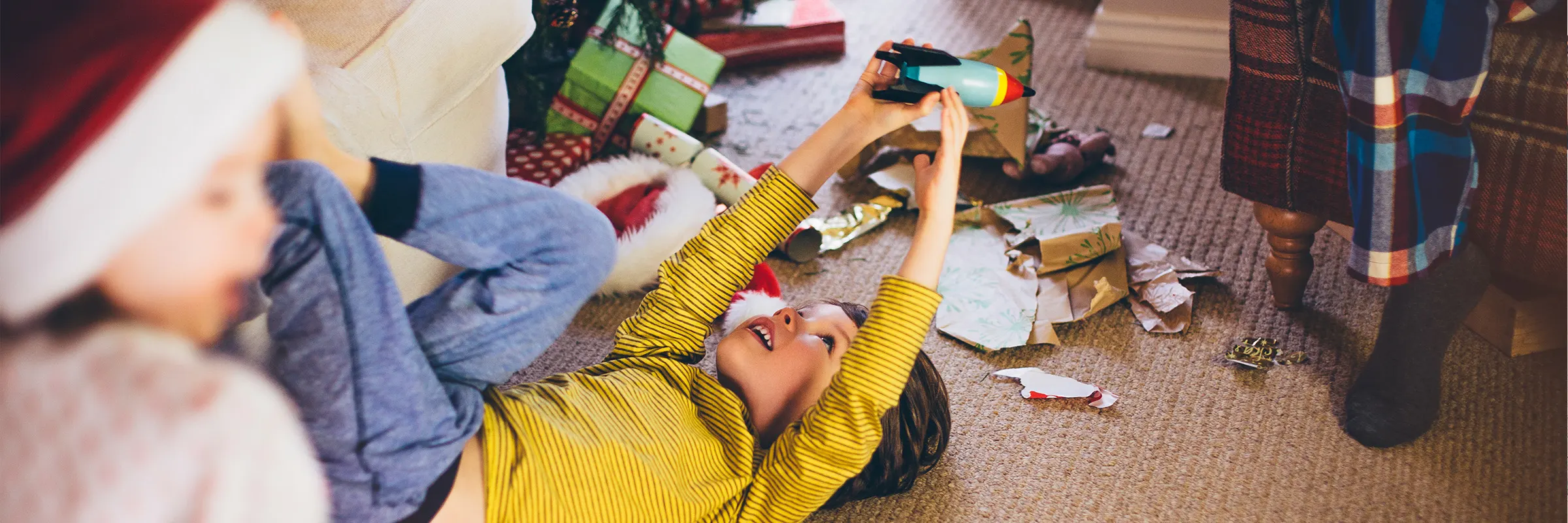 A boy plays with a new toy while surrounded by wrapping paper