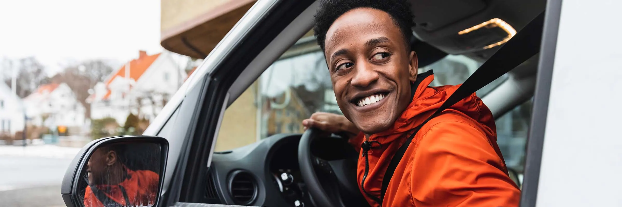 A young man is sitting in a van and looking out the driver&rsquo;s side window while smiling.