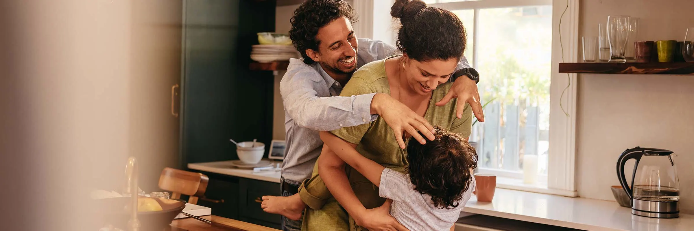 A mother and father are playing with their child in the kitchen of their home.