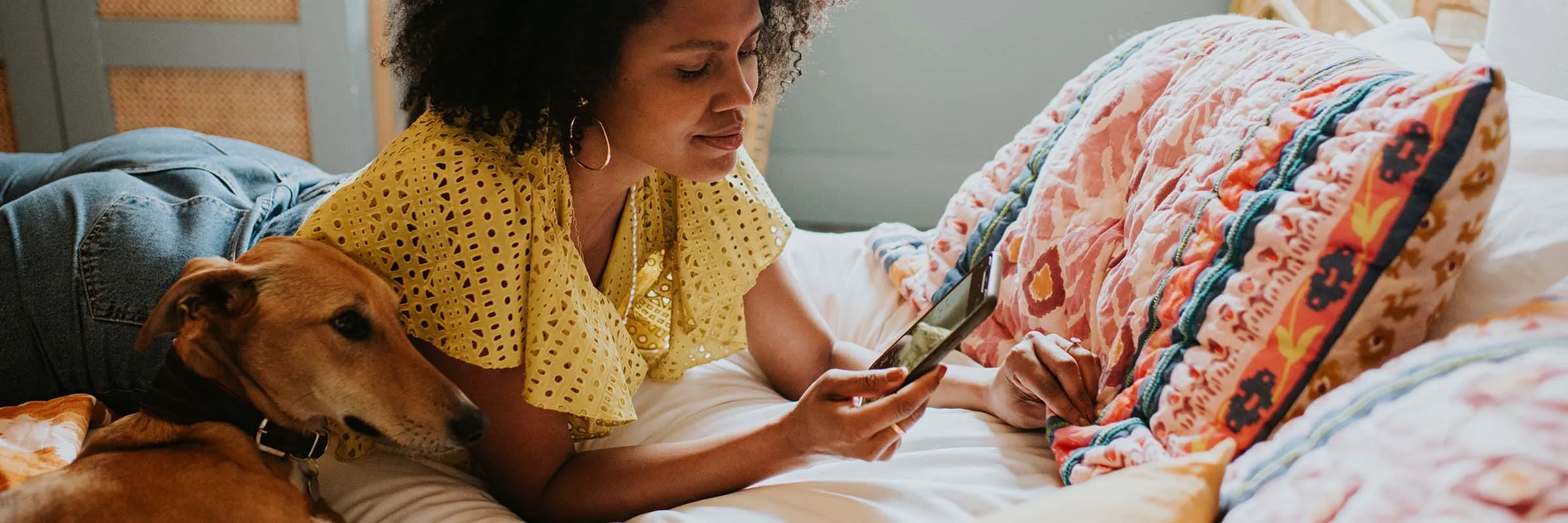 Image of a woman looking at her phone while lounging on her bed with her dog