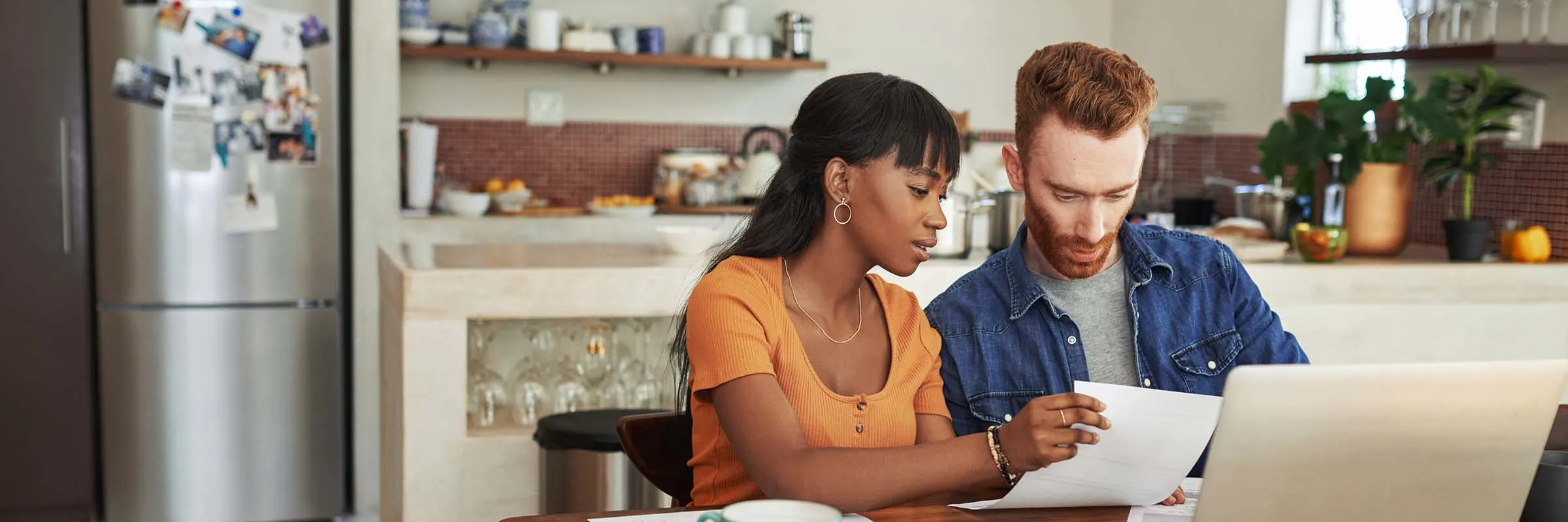 Couple at a kitchen table with paperwork, a calculator and a laptop