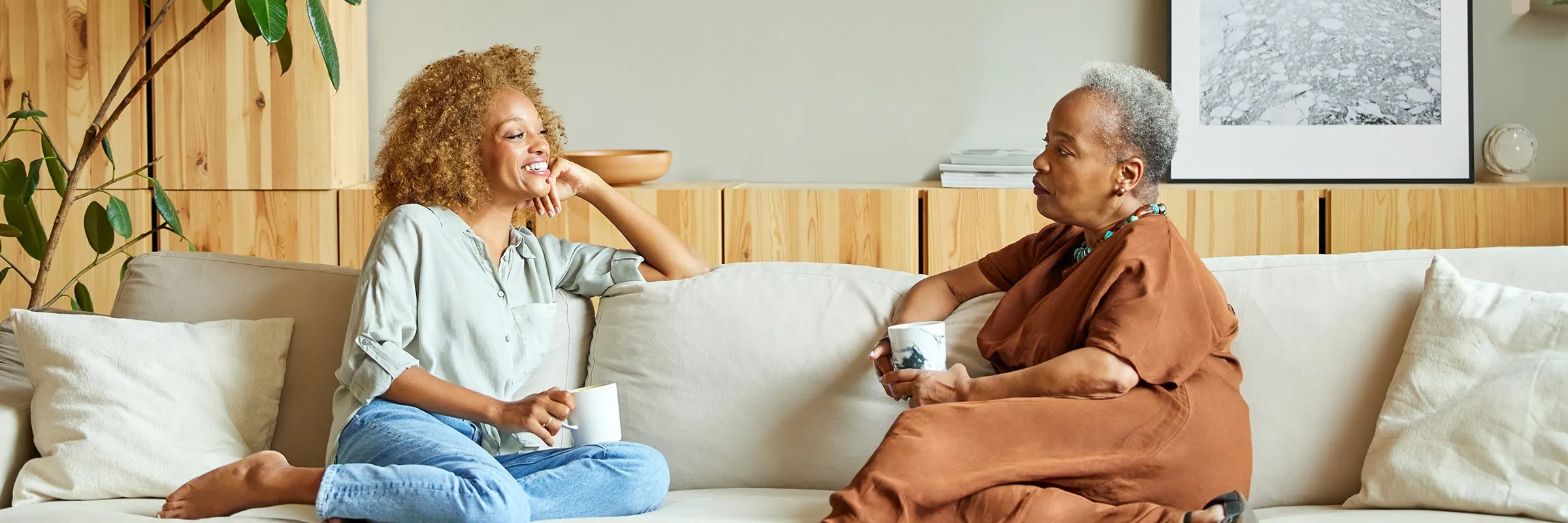 Mother and daughter sitting on a mid century modern couch chatting with coffee in their hands