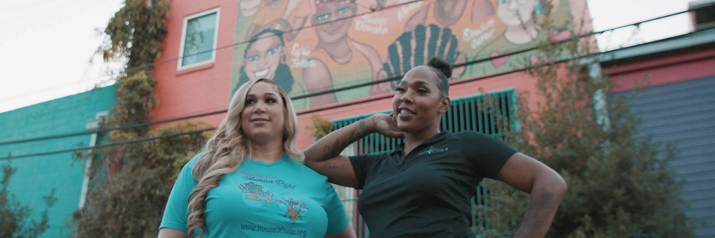 Alt text: Mariah Moore and her co-founder of House of Tulip pose outside the building under a mural