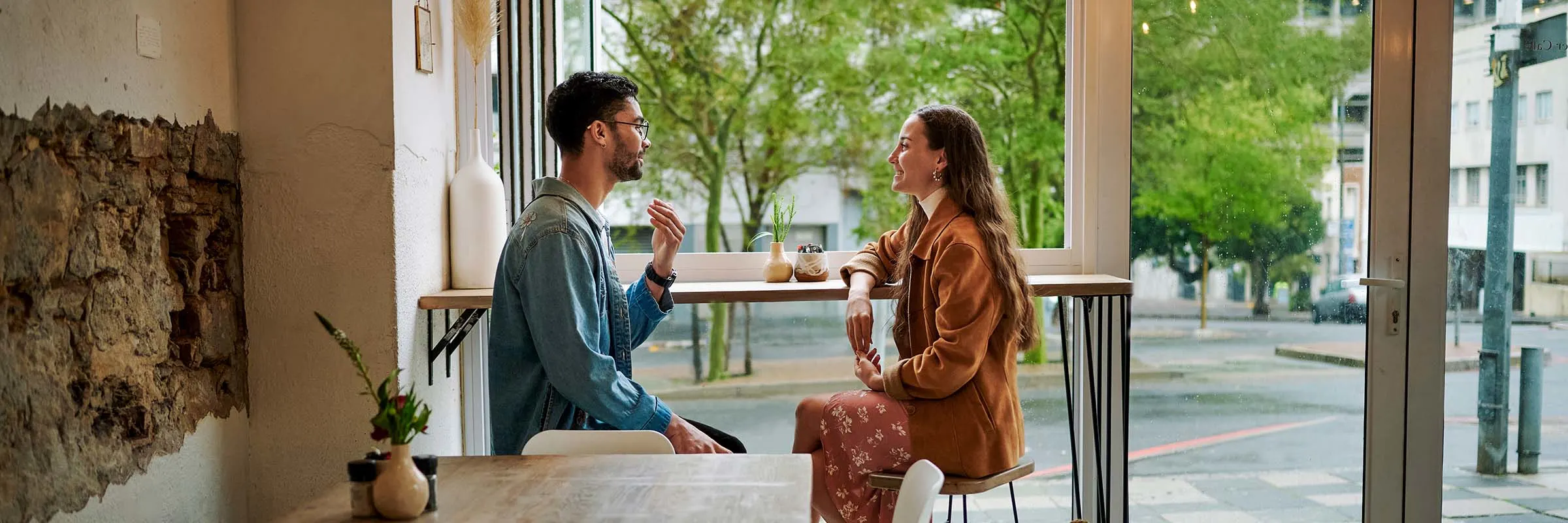 Two adults have a conversation inside a cafe on a sunny day.