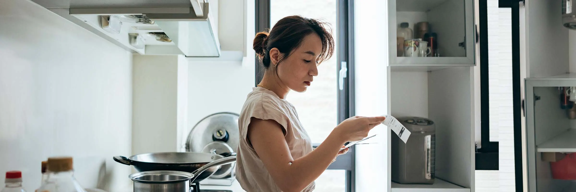 Woman stands at the kitchen counter going over a bill