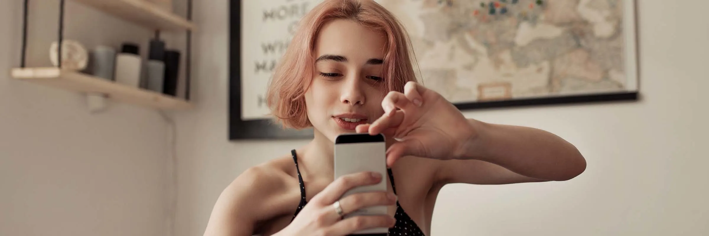 Woman sits on her bed in her room, looking at her phone.