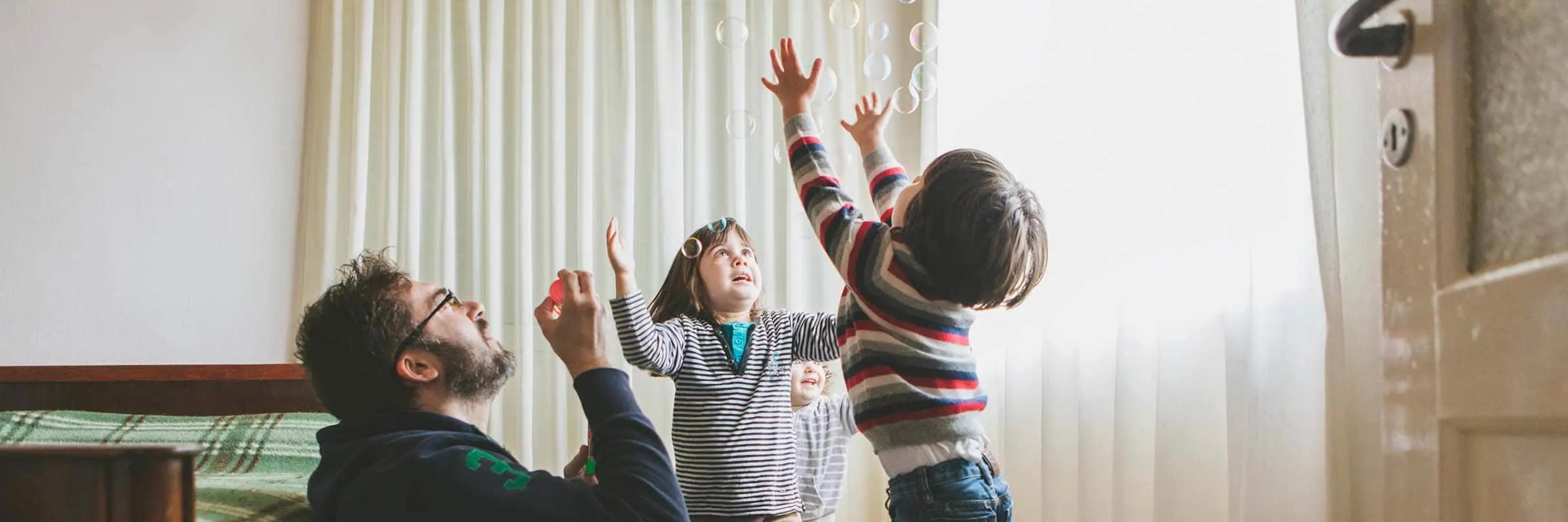 Image of a man blowing bubbles in bedroom with his three kids.