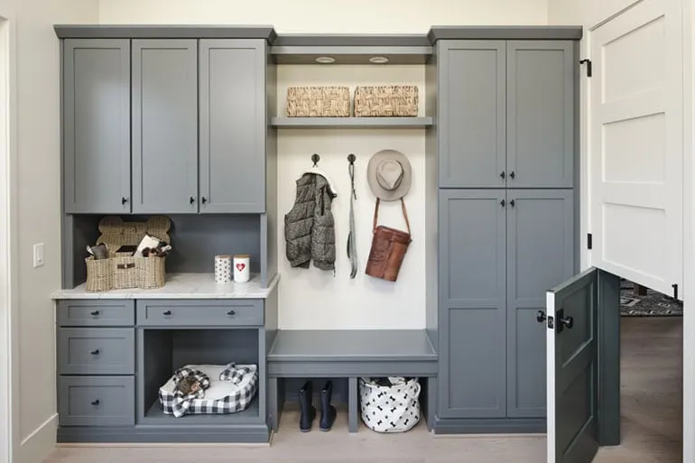 Photo shows cabinetry in a mudroom with a Dutch door to allow pets easy access. Items like a hat and vest hang on the wall.