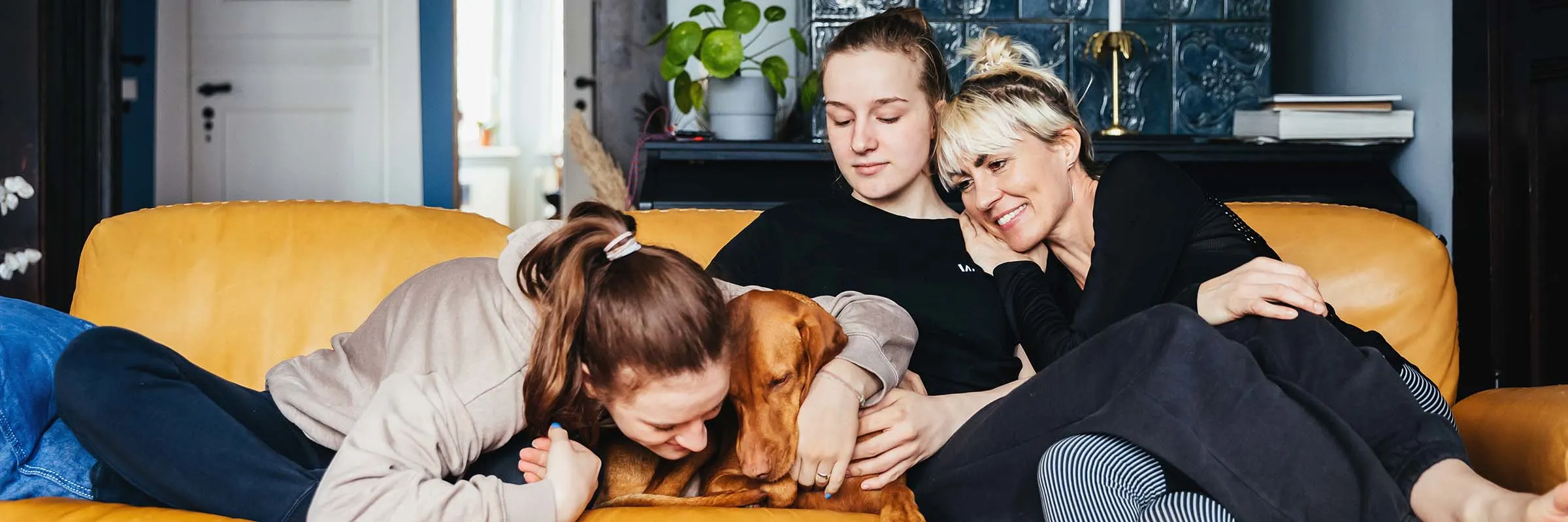 Single mom sitting on sofa with daughters and family dog.