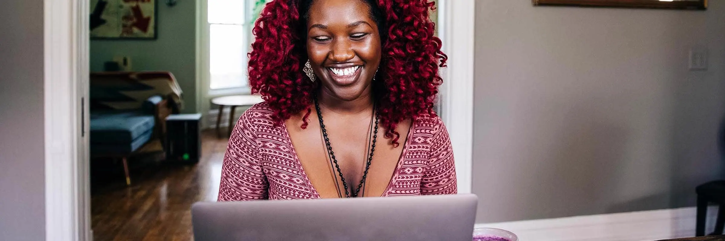 Smiling young woman sitting at a table while working on a laptop.