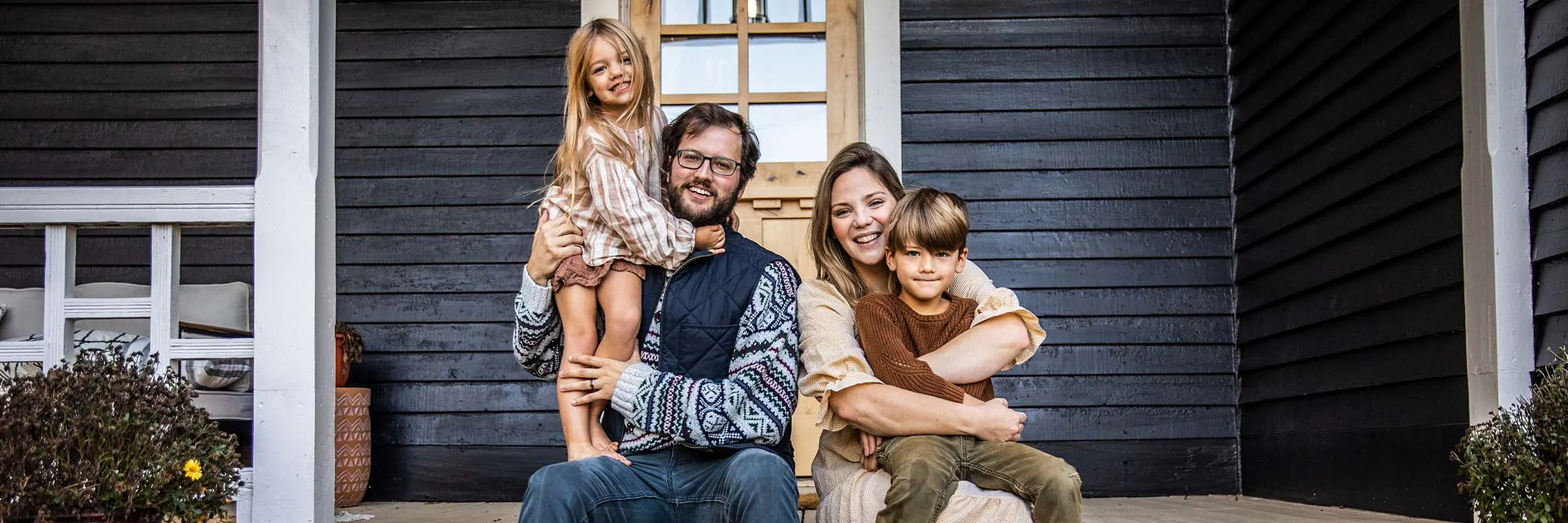 A family poses for a portrait on the front porch steps of a farmhouse.