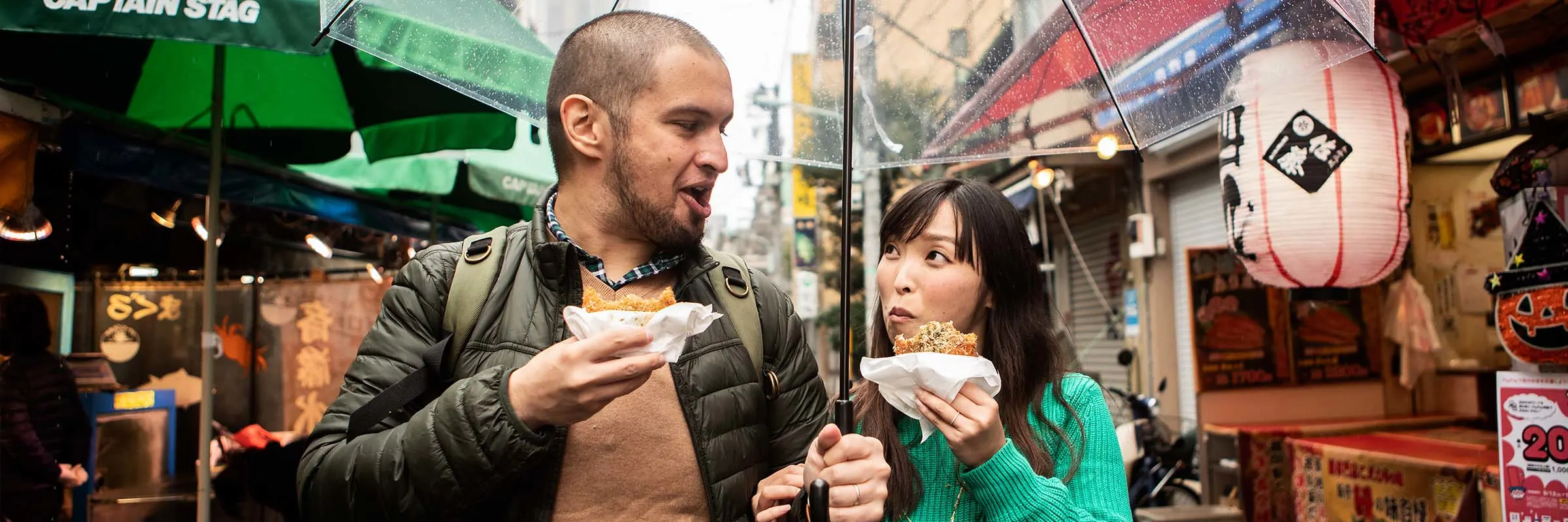 A married couple walks through a city street sightseeing while eating