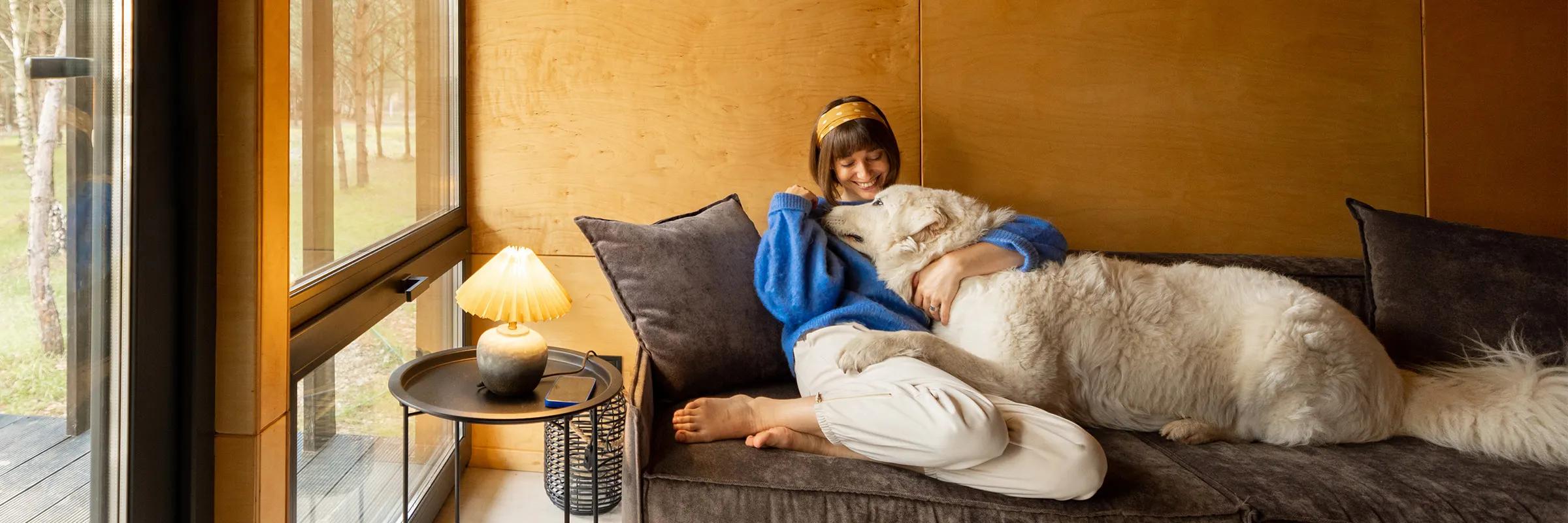 Woman sitting on the couch smiling with her dog in her lap.