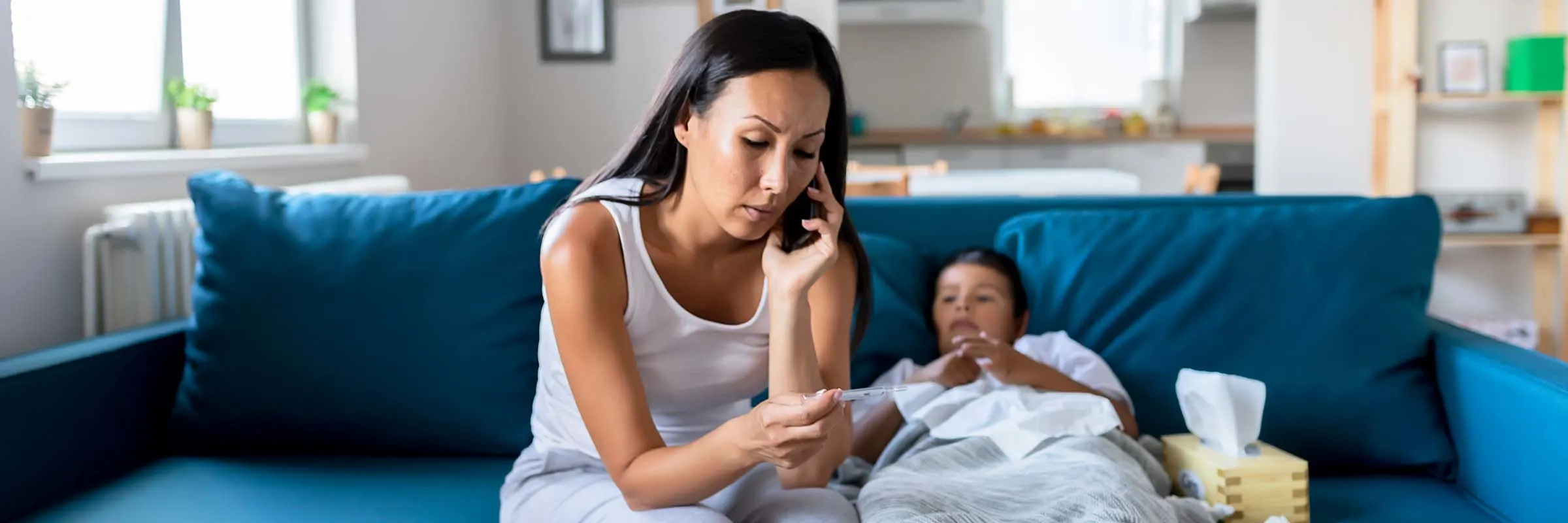 Woman holding a thermometer while on the phone and a sick child next to her.