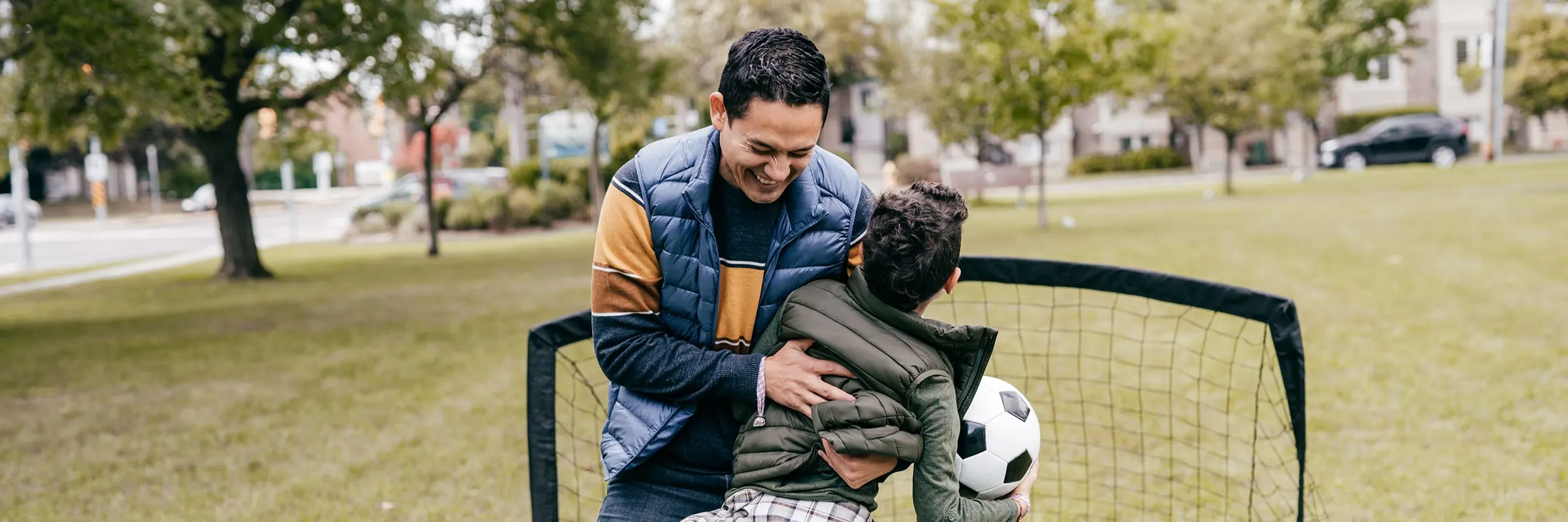 A happy father hugs his son while they play soccer in a park.