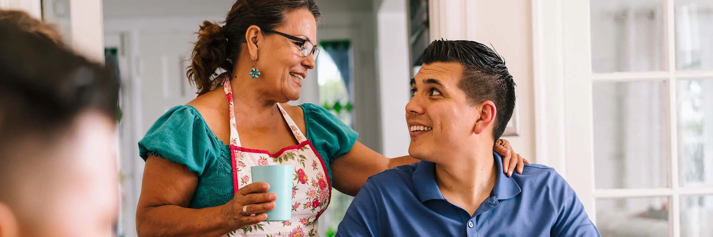Young man sits at a dinner table with his family and looks at his mother, who is smiling.