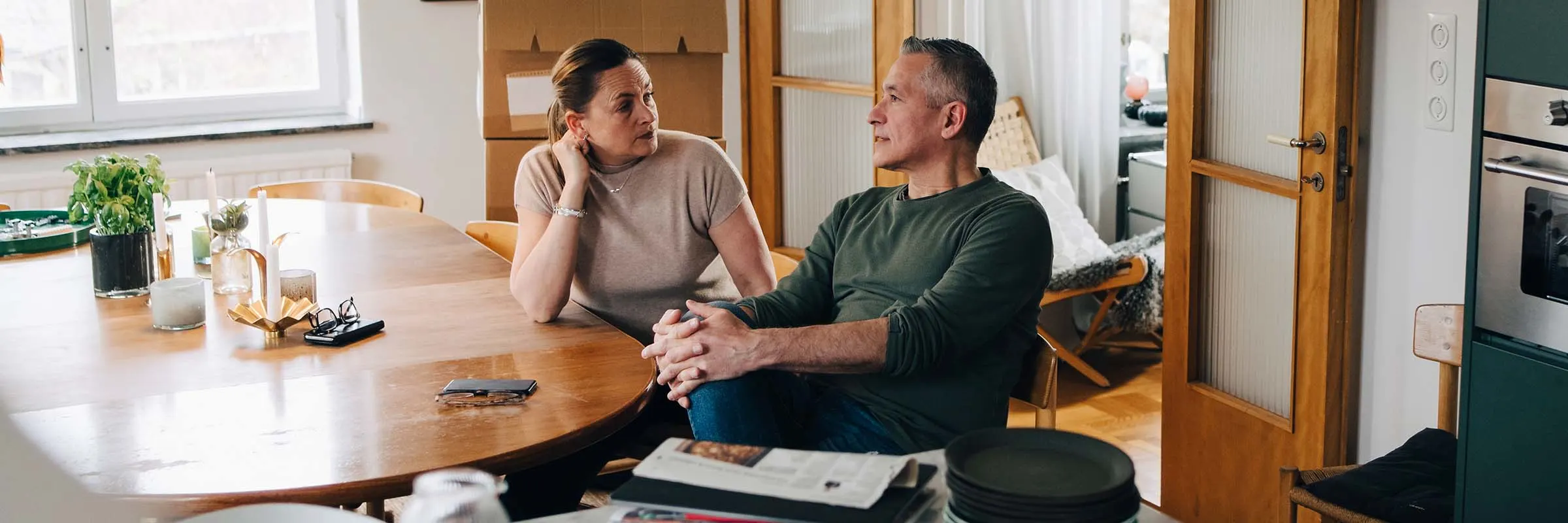 A woman and man sit at their dining room table while having a conversation.