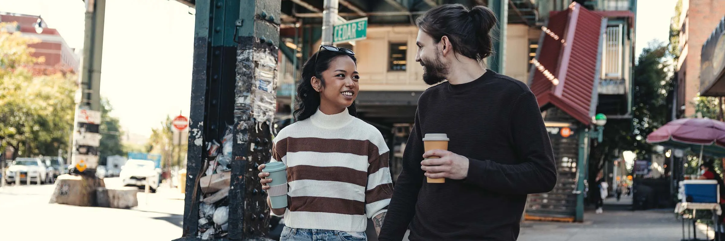 Couple walking down city street together with coffees in hand.