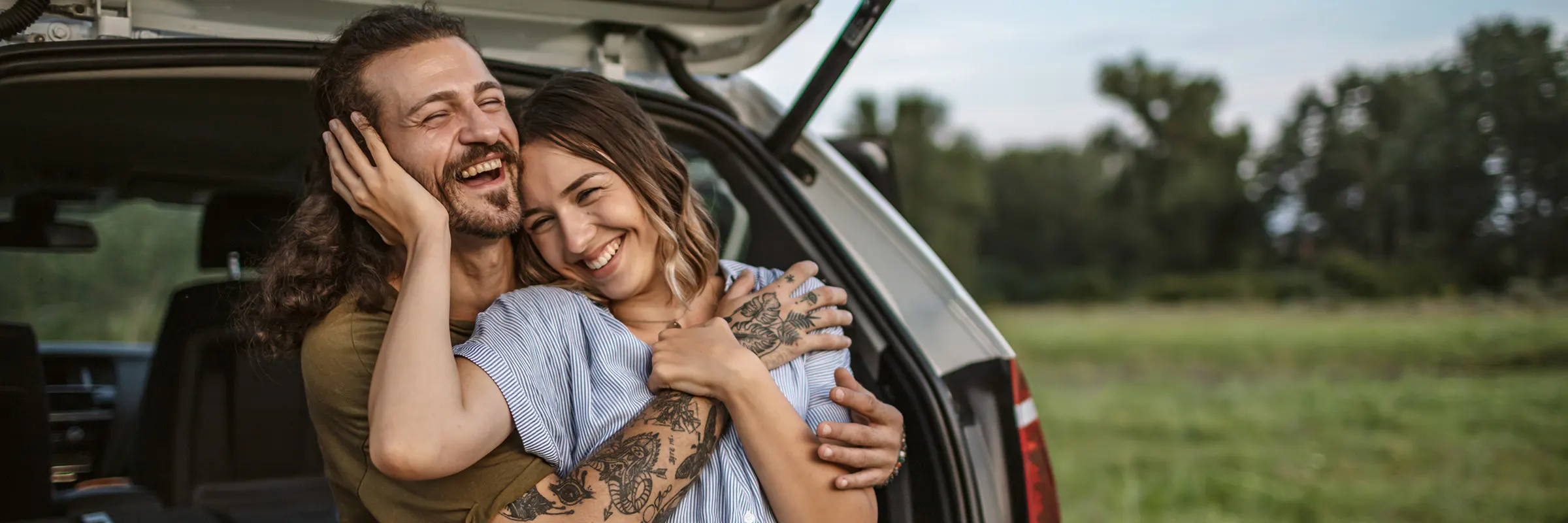 Couple embracing and laughing together while sitting in the trunk of the car.