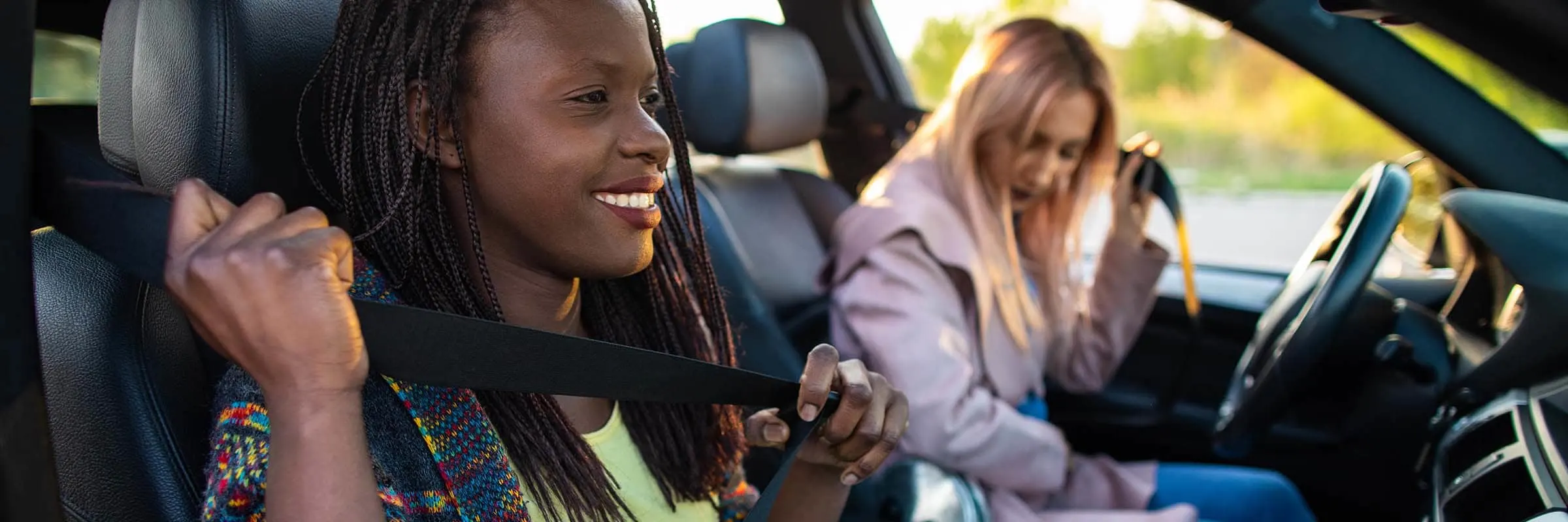 Two women in in a car buckling their seatbelts.