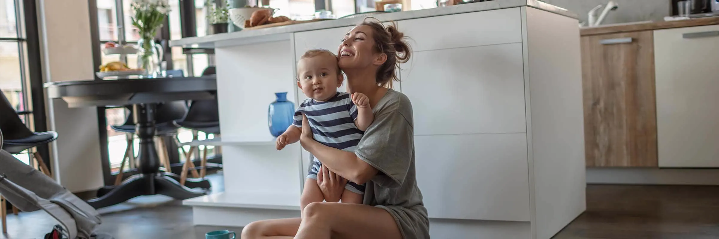 A woman is sitting on the floor in her kitchen playing with her baby.