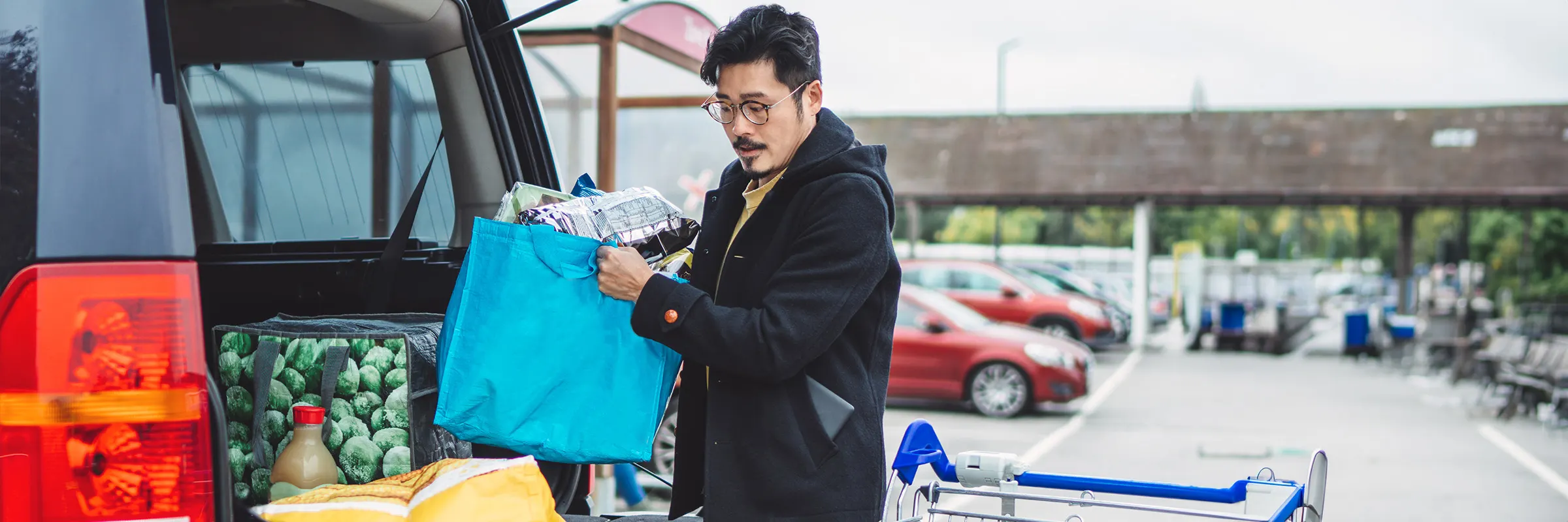 A man loads bagged groceries into the truck of his car.