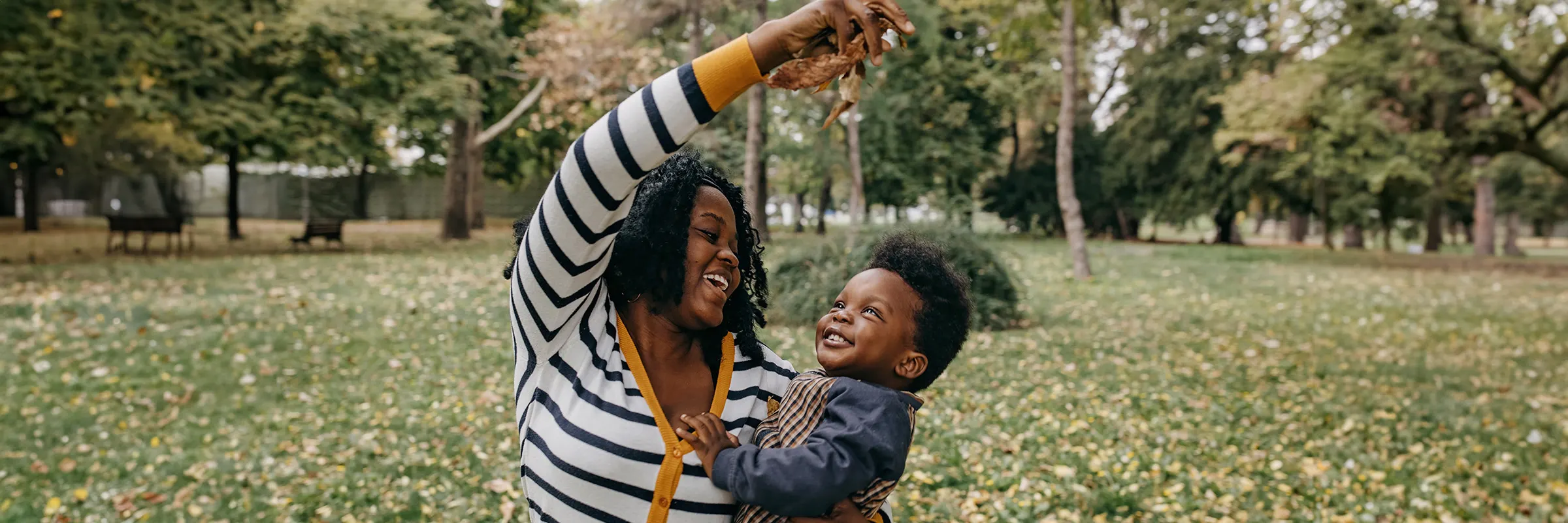 A woman plays in the leaves with her young son outside.