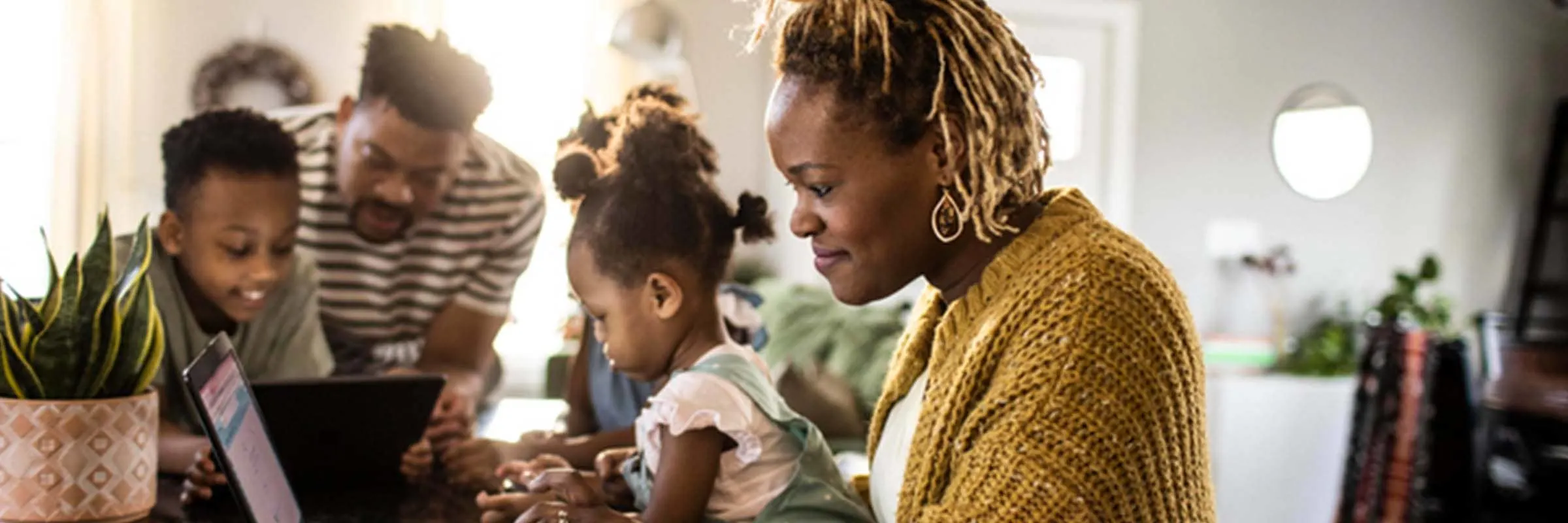 A mother sitting at her kitchen counter working on her computer with her husband, son and daughter