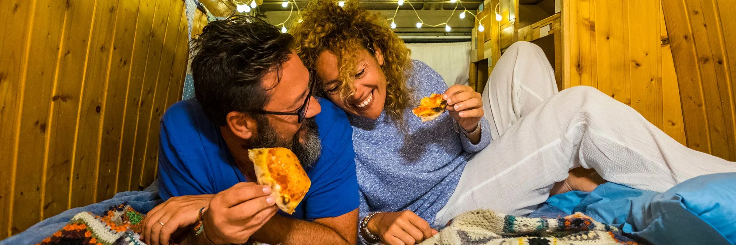 Man and woman laying down laughing and eating pizza.