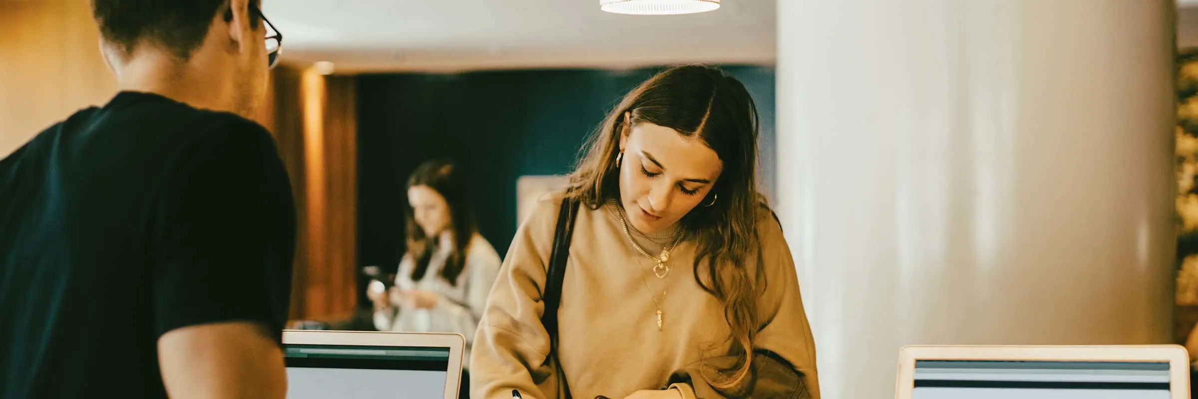 Man looking at woman signing at reception desk in hotel lobby