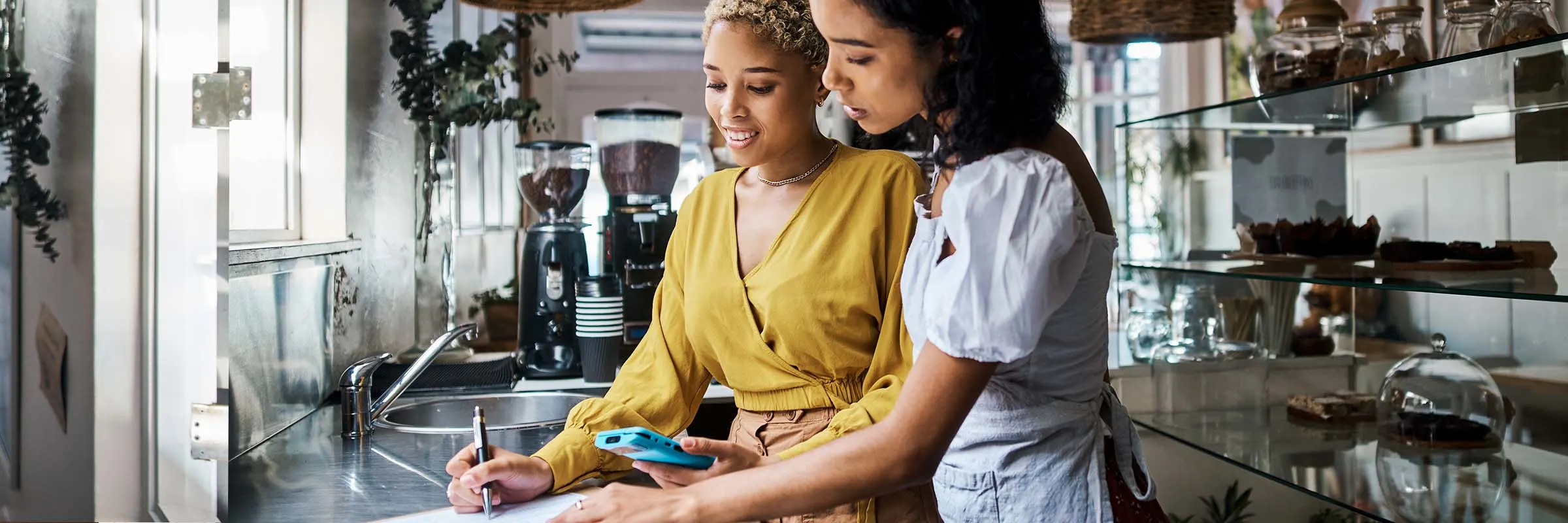 Two women taking notes on a clipboard in a kitchen.