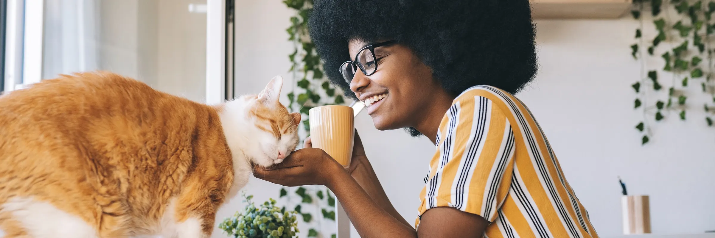  Woman sips her coffee at a table while petting her orange cat