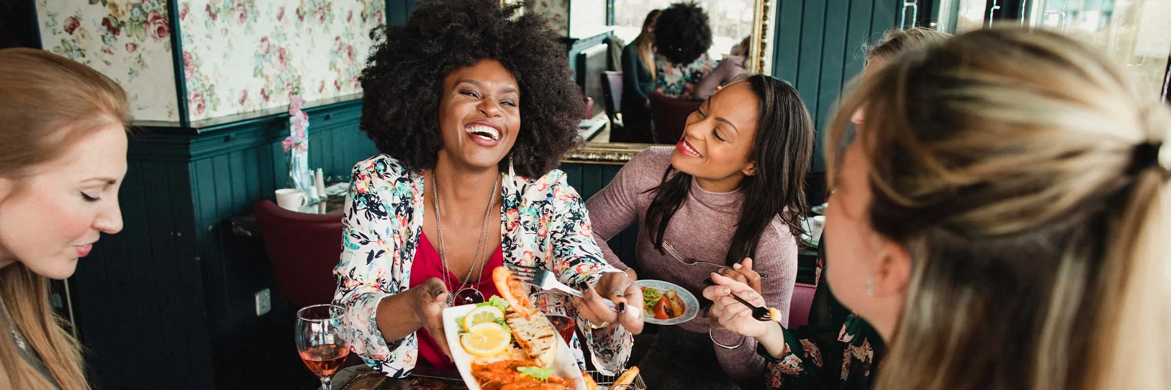 A group of four female friends laughing and sharing appetizers together at a trendy restaurant