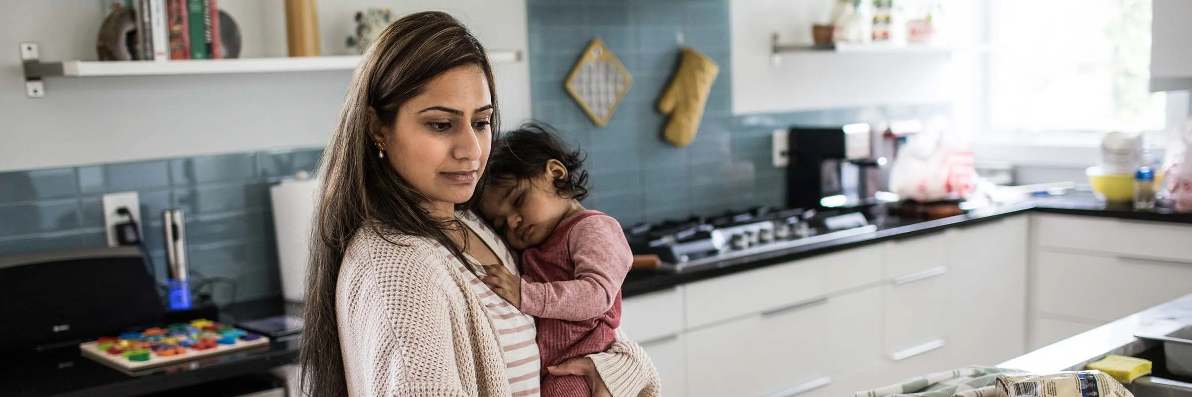 Mother holding baby and multi-tasking in kitchen