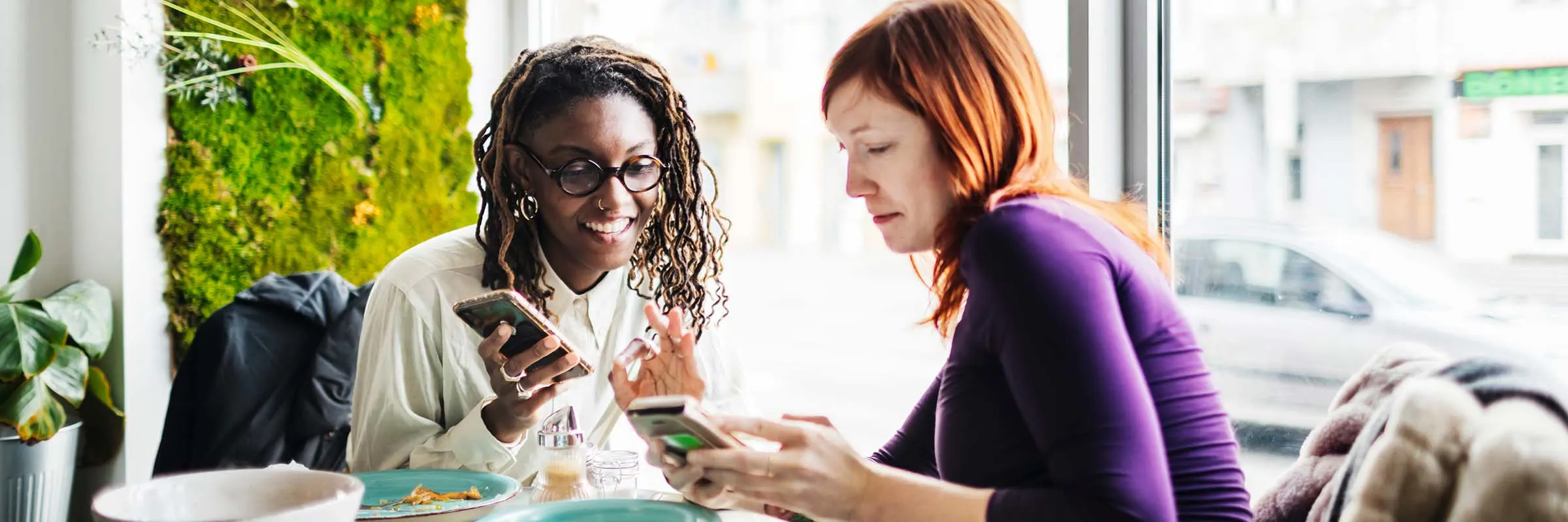 Two friends looking at their smartphones in a caf&eacute;