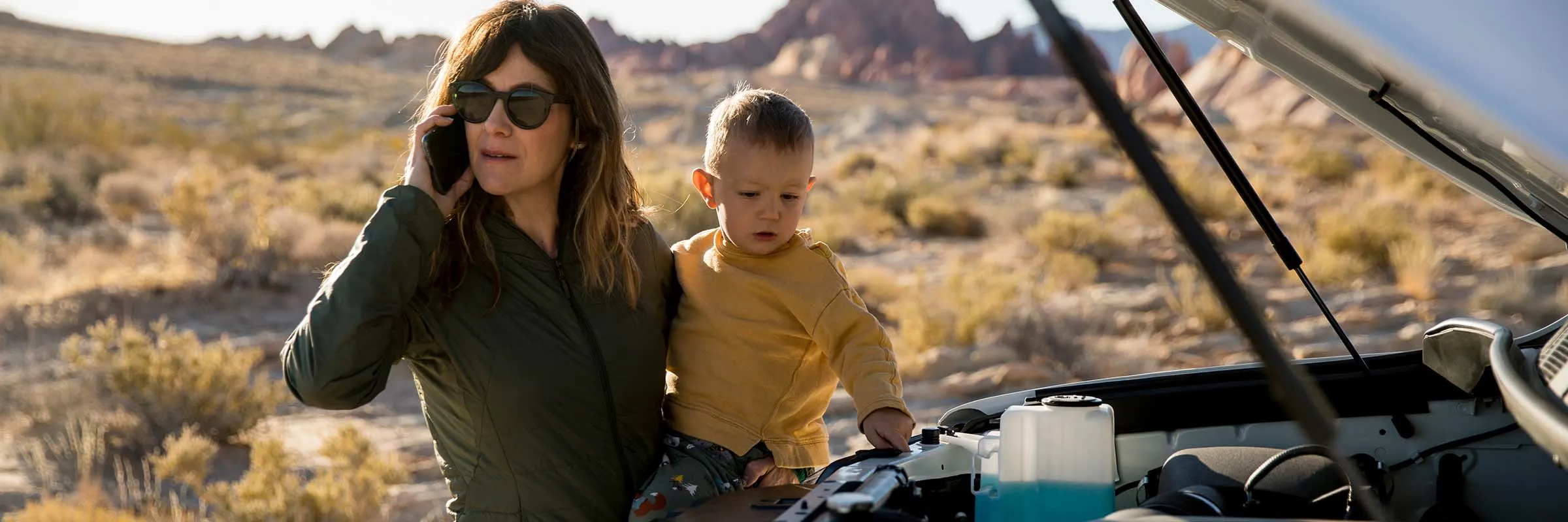 A woman on the phone having car trouble with child in arms.