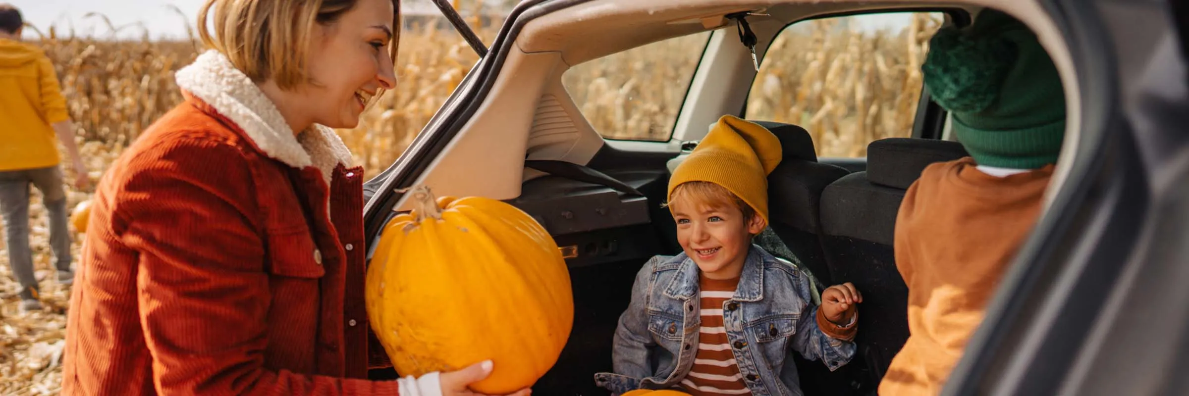 A mother and her two children loading pumpkins into the trunk of her vehicle.