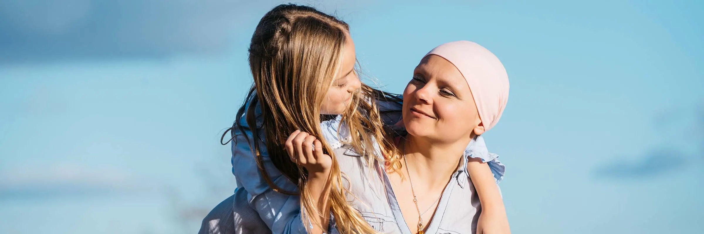 A woman fighting cancer is carrying her daughter on her back and smiling.