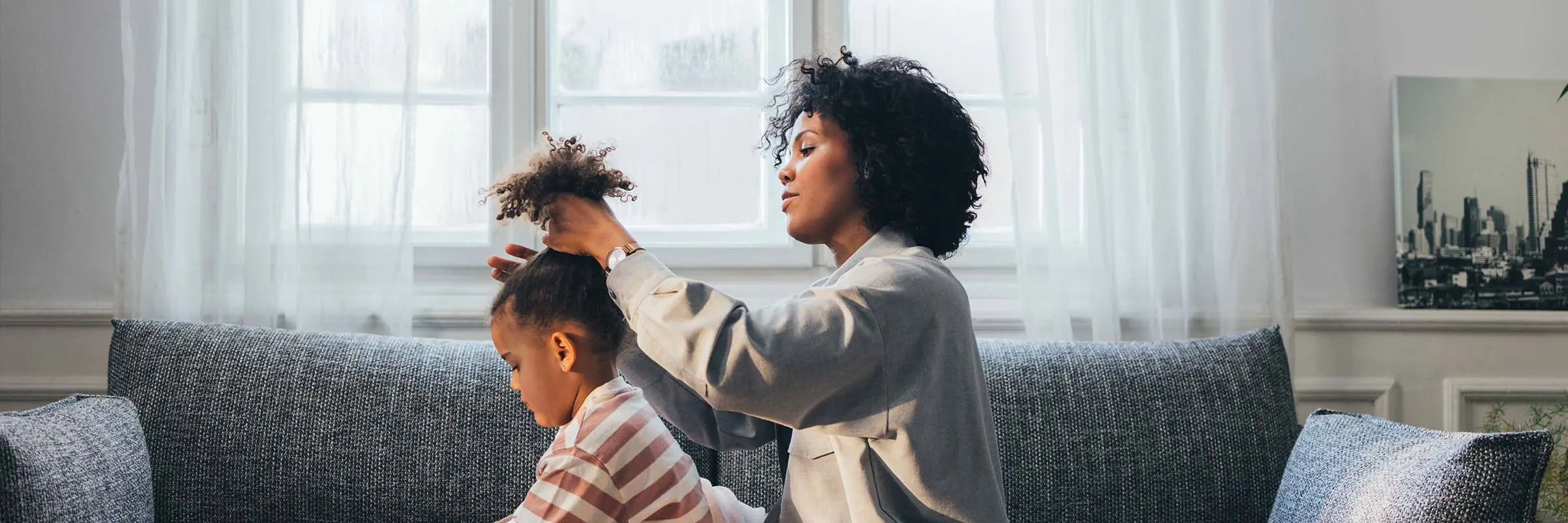 A woman does her daughter's hair while sitting on the couch