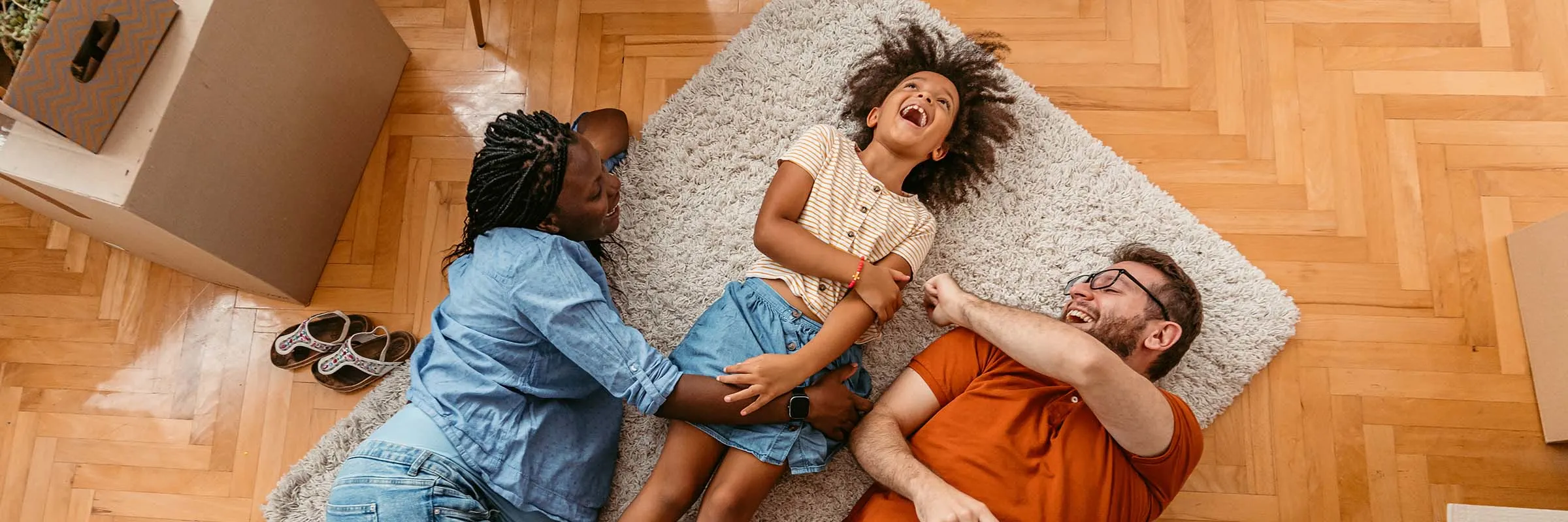 A mother, daughter and father are lying on the floor of their new dining room. They are surrounded by moving boxes.