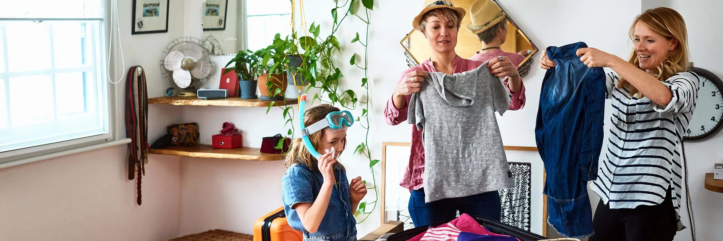 Couple packing their clothes for an upcoming trip while daughter wearing snorkeling gear helps