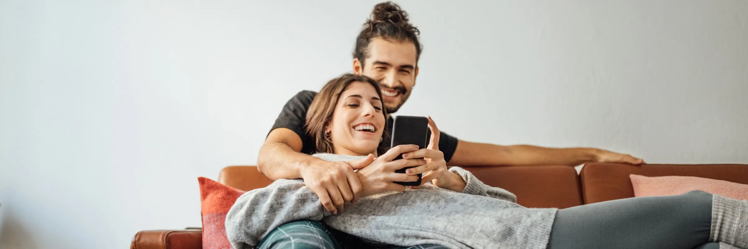 Couple sitting on couch together laughing while looking at phone